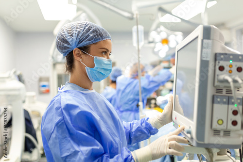 Anesthesiologist keeping track of vital functions of the body during cardiac surgery. Surgeon looking at medical monitor during surgery. Doctor checking monitor for patient health status. photo