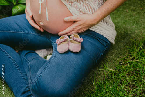 Mujer embarazada sentada sobre césped con zapatitos de bebe photo