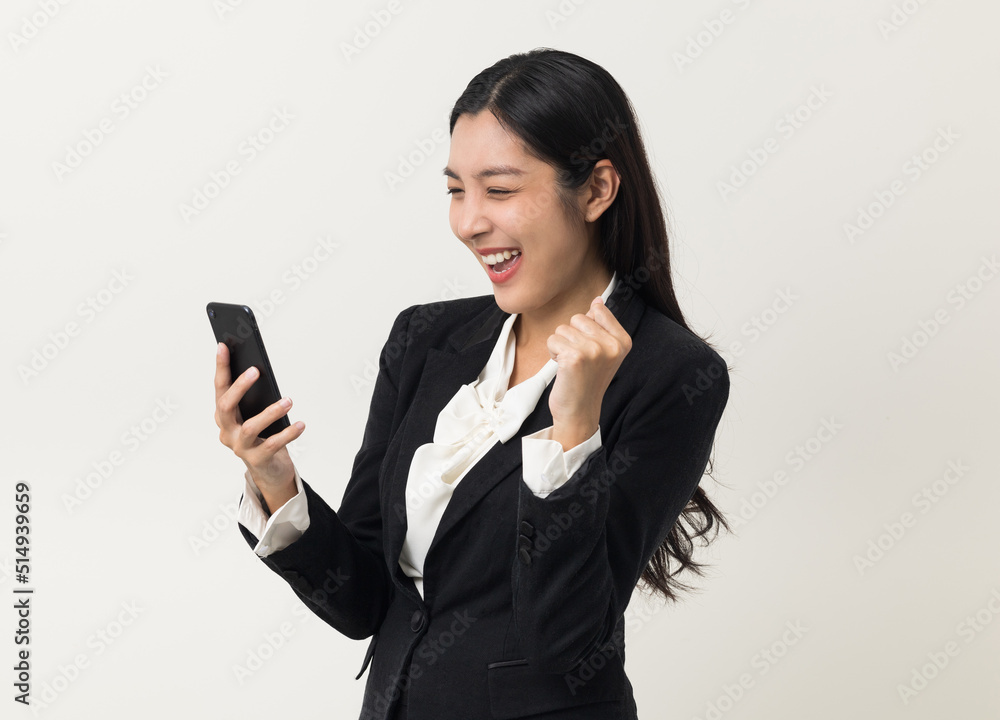 Happy young asian business woman using smartphone on isolated white background. Attractive female in suit holding cell phone feeling happy. Portrait shot in studio. Happy young asian business woman using smartphone on isolated white background. Attractive female in suit holding cell phone feeling happy. Portrait shot in studio.
