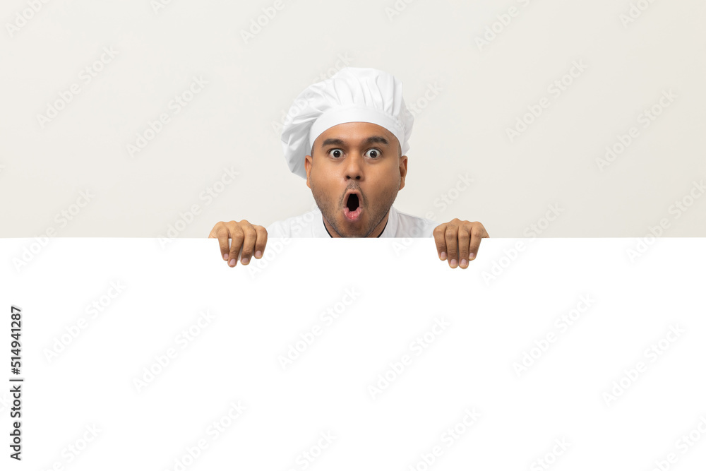 Happy Young handsome asian man chef in uniform looks out from behind an empty whiteboard. Cooking indian man hiding behind big blank billboard for advertising text menu in kitchen and restaurant. Happy Young handsome asian man chef in uniform looks out from behind an empty whiteboard. Cooking indian man hiding behind big blank billboard for advertising text menu in kitchen and restaurant.