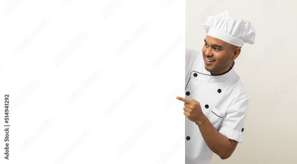 Happy Young handsome asian man chef in uniform looks out from behind an empty whiteboard. Cooking indian man hiding behind big blank billboard for advertising text menu in kitchen and restaurant. Happy Young handsome asian man chef in uniform looks out from behind an empty whiteboard. Cooking indian man hiding behind big blank billboard for advertising text menu in kitchen and restaurant.