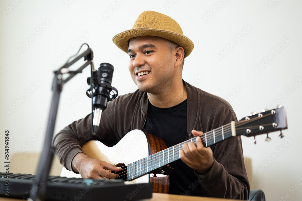Obraz premium Lifestyle concept. Young asian musician playing guitar in living room at home on this weekend. Relaxing with sing a song. Asian man having fun playing acoustic guitar