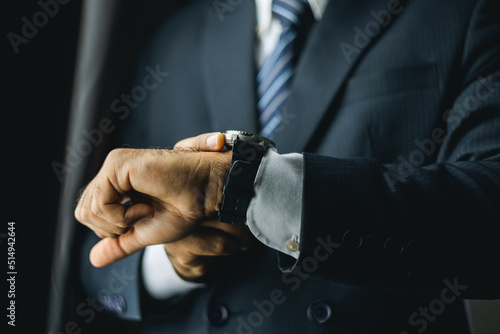 Confident businessman in classic blue suit wearing or adjust watch with necktie near window in hotel room. Handsome man wearing a nice suit on wedding day. © Chanakon