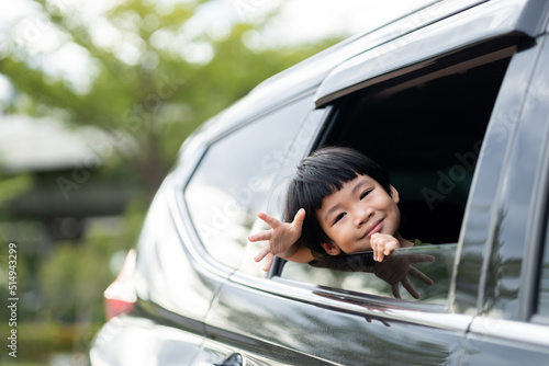 Happy asian boy waving hands gesturing hello out of the car window during a trip with his family. Little child sticking head outta the windshield traveling in a car on a summer vacation. photo