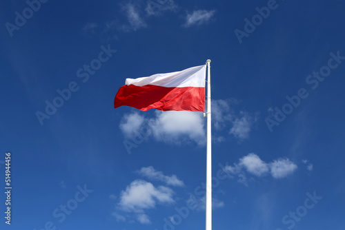 The red and white flag of Poland flutters against a bright blue sky with clouds. Independence Day of Poland. Freedom and Democracy
