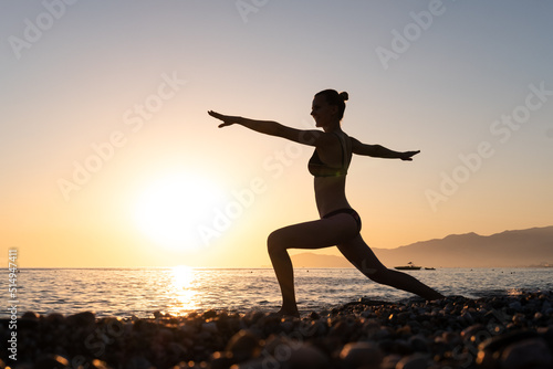 Yoga wellness retreat class on morning sunrise beach landscape. Silhouette of girl standing in warrior pose meditation vertical background.