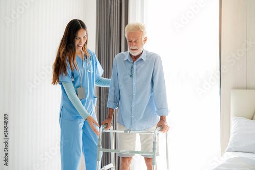 Care worker helping elderly man get out of bed and walk around the room.