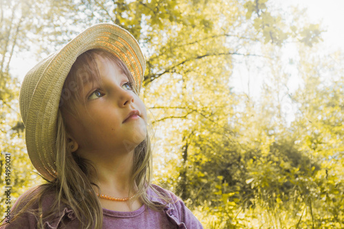 A girl with a cap on her head, a purple dress looks up against the background of an autumn forest. Little blonde girl on a walk