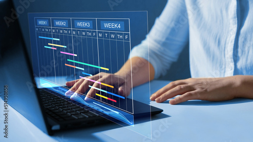  Project manager working on laptop and updating tasks and milestones progress planning with Gantt chart scheduling interface for company on virtual  screen. Business Data Management System.