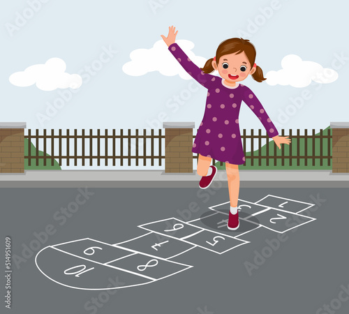 Cute little girl playing hopscotch drawn with chalk outside on playground street at the park
