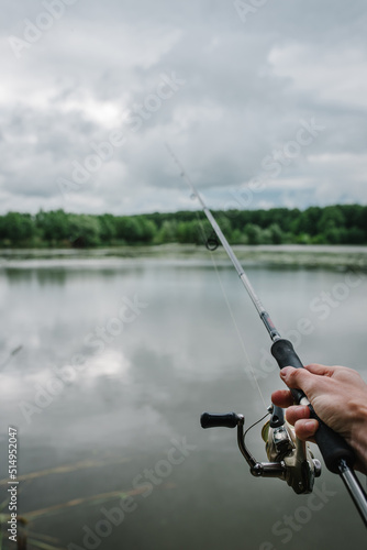 Fisherman with rod, spinning reel on the river bank. Fishing for pike, perch, carp. Fog against the backdrop of lake. Background misty morning. wild nature. Article about fishing day.