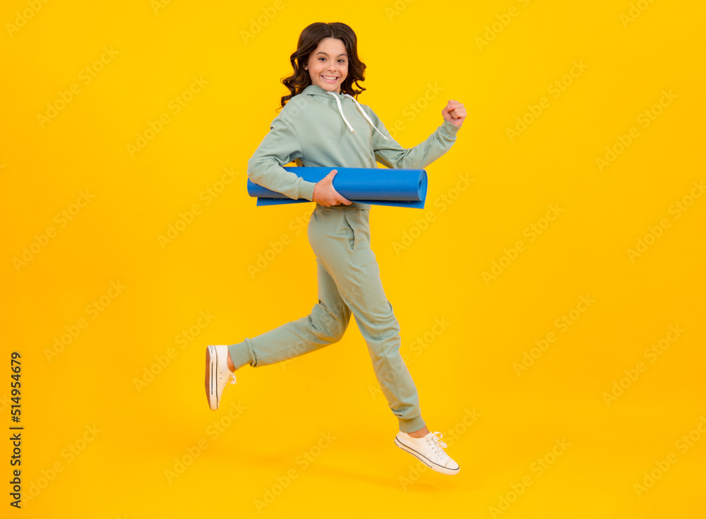 Sportswear advertising concept. Run and jump. Teenager child girl in tracksuits jogging suit posing in the studio hold fitness mat.
