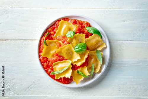 A plate of ravioli with tomato sauce and basil, simple Italian meal, shot from above on a rustic wooden background