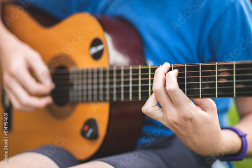 Close-up of hands of guy playing guitar. The man's hands tug on the strings of the acoustic guitar.