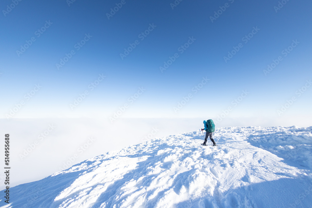 A woman with a backpack in snowshoes climbs a snowy mountain