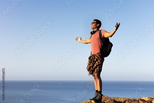 Young man standing on the stone with raised up arms. Tourist man on the top of the mountain. © JustLife