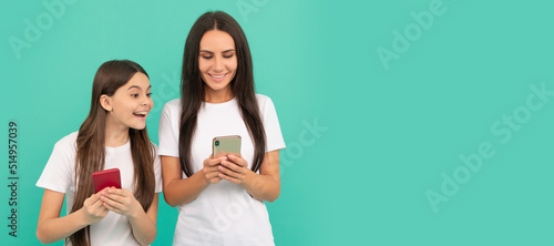 Mother and daughter child banner, copy space, isolated background. surprised mother and daughter chatting on smartphone on blue background.