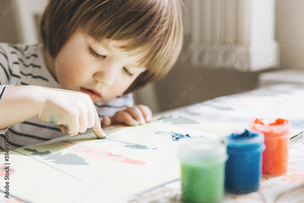 Finger painting. Portrait of cute little boy painting with fingers at home. Close-up of child's hand in colorful paints. Early education concept. Sensory play. Development of fine motor skills. Finger painting. Portrait of cute little boy painting with fingers at home. Close-up of child's hand in colorful paints. Early education concept. Sensory play. Development of fine motor skills.