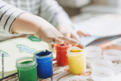 Finger painting. Cute little boy painting with fingers at home. Close-up of child's hand in colorful paints. Early education concept. Sensory play. Development of fine motor skills. © Lyubov