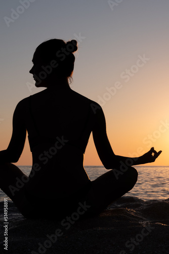 Silhouette of woman yoga in Lotus position on the shore of ocean at evening.