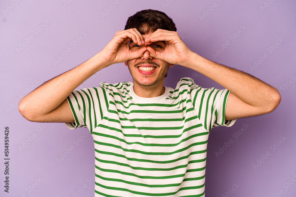 Young caucasian man isolated on purple background showing okay sign over eyes Young caucasian man isolated on purple background showing okay sign over eyes