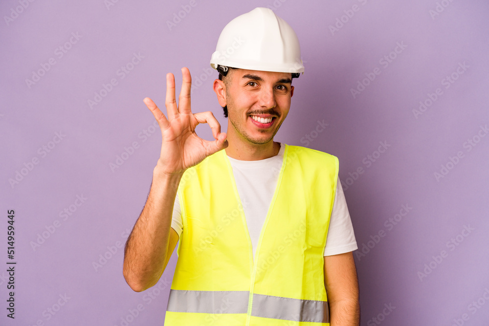 Young hispanic worker man isolated on purple background cheerful and confident showing ok gesture.