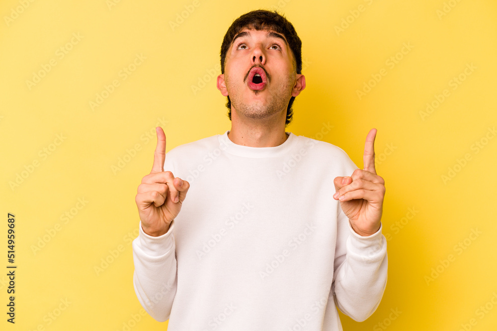 Young caucasian man isolated on yellow background pointing upside with opened mouth. Young caucasian man isolated on yellow background pointing upside with opened mouth.