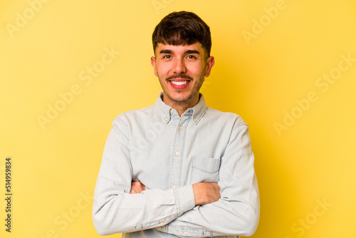Young caucasian man isolated on yellow background who feels confident, crossing arms with determination.