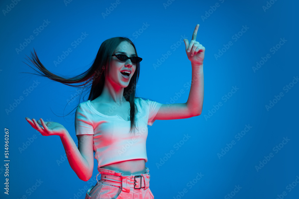 Half-length shot of emotional girl with long glossy dark hair isolated on blue background in neon light. Concept of beauty, art, fashion, emotions Half-length shot of emotional girl with long glossy dark hair isolated on blue background in neon light. Concept of beauty, art, fashion, emotions