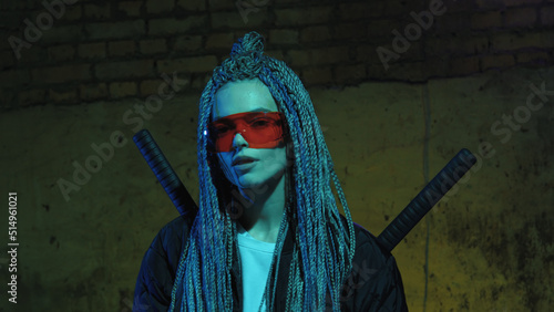 girl with dreadlocks and katanas in red glasses posing against a neon brick wall photo