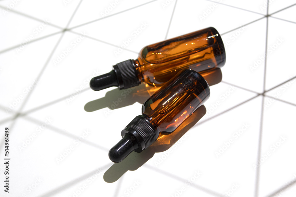 Amber glass dropper bottles different sizes with geometric shadow on white background. Hyaluronic acid oil, serum with collagen and peptides skin care product. Amber glass dropper bottles different sizes with geometric shadow on white background. Hyaluronic acid oil, serum with collagen and peptides skin care product.