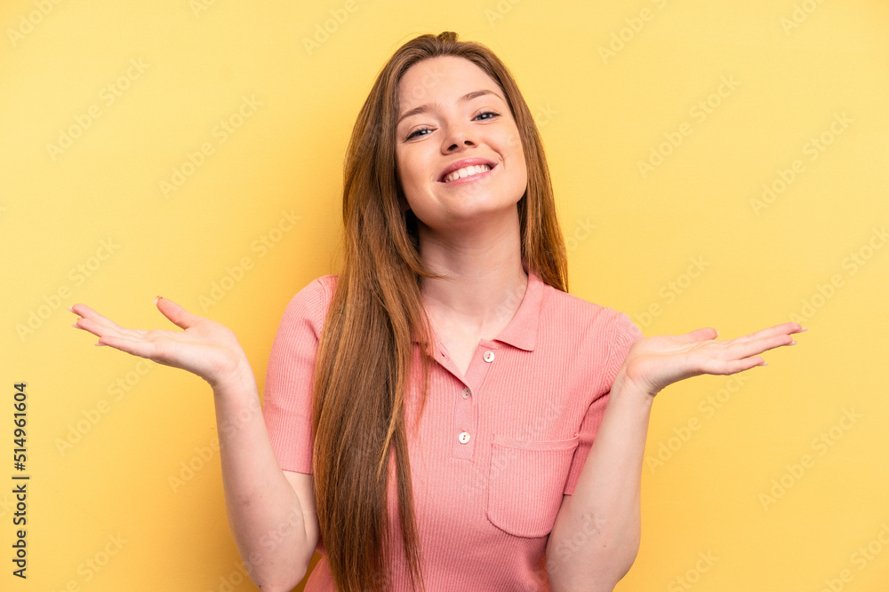 Young caucasian woman isolated on yellow background makes scale with arms, feels happy and confident. Young caucasian woman isolated on yellow background makes scale with arms, feels happy and confident.