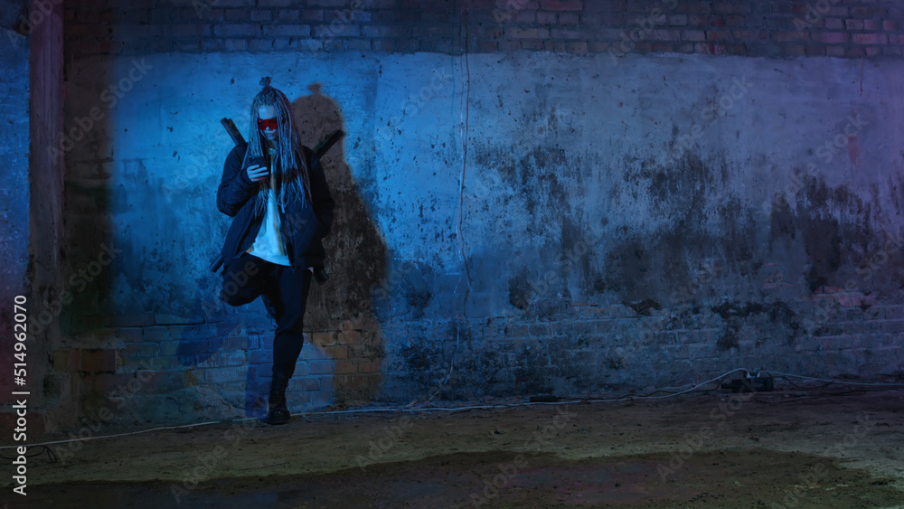 a girl with dreadlocks and katanas in red glasses is texting on a mobile phone against a neon brick wall