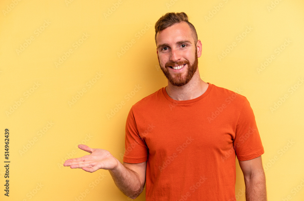 Young caucasian man isolated on yellow background showing a copy space on a palm and holding another hand on waist. Young caucasian man isolated on yellow background showing a copy space on a palm and holding another hand on waist.