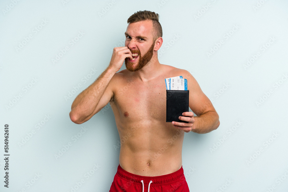 Fototapeta premium Young caucasian man holding a passport isolated on blue background biting fingernails, nervous and very anxious.