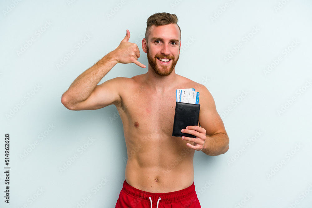 Fototapeta premium Young caucasian man holding a passport isolated on blue background showing a mobile phone call gesture with fingers.
