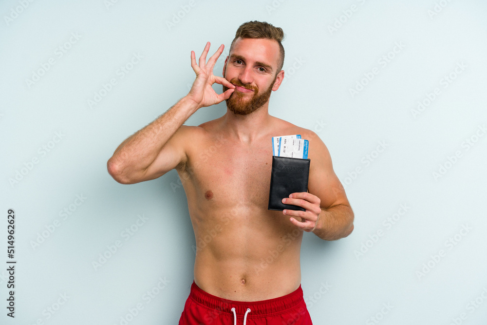 Fototapeta premium Young caucasian man holding a passport isolated on blue background with fingers on lips keeping a secret.