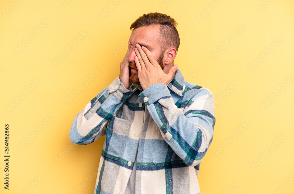 Young caucasian man isolated on yellow background afraid covering eyes with hands. Young caucasian man isolated on yellow background afraid covering eyes with hands.
