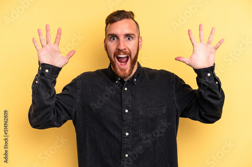 Young caucasian man isolated on yellow background receiving a pleasant surprise, excited and raising hands. © Asier