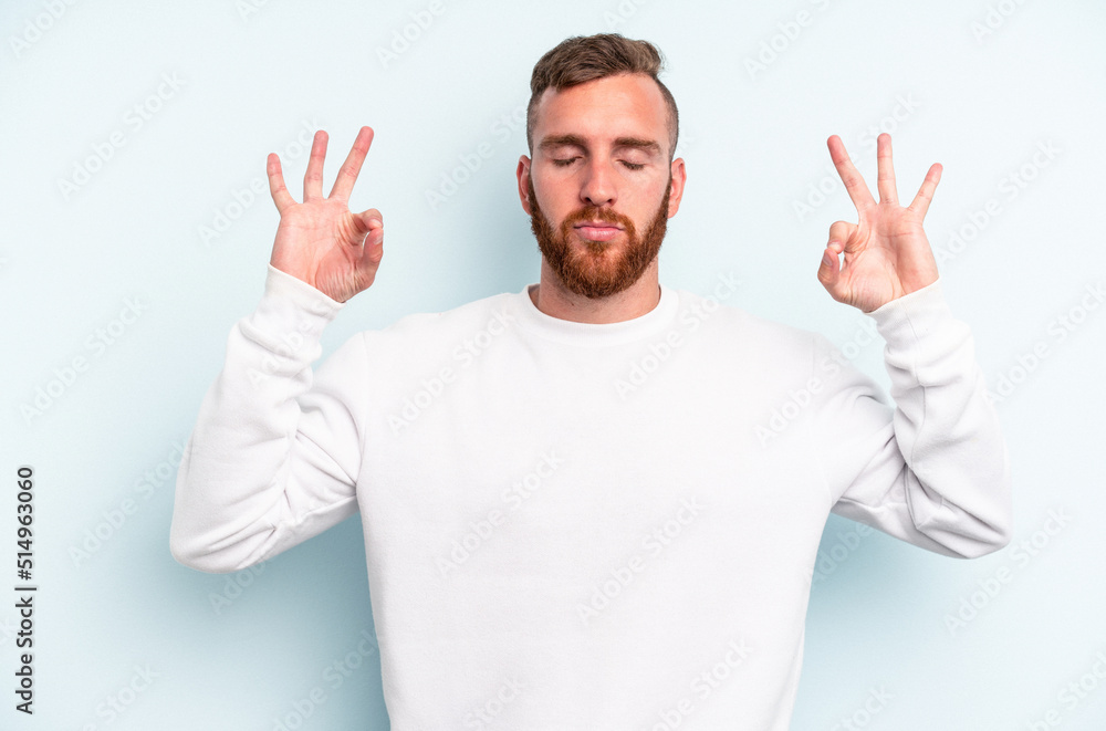Young caucasian man isolated on blue background relaxes after hard working day, she is performing yoga. Young caucasian man isolated on blue background relaxes after hard working day, she is performing yoga.