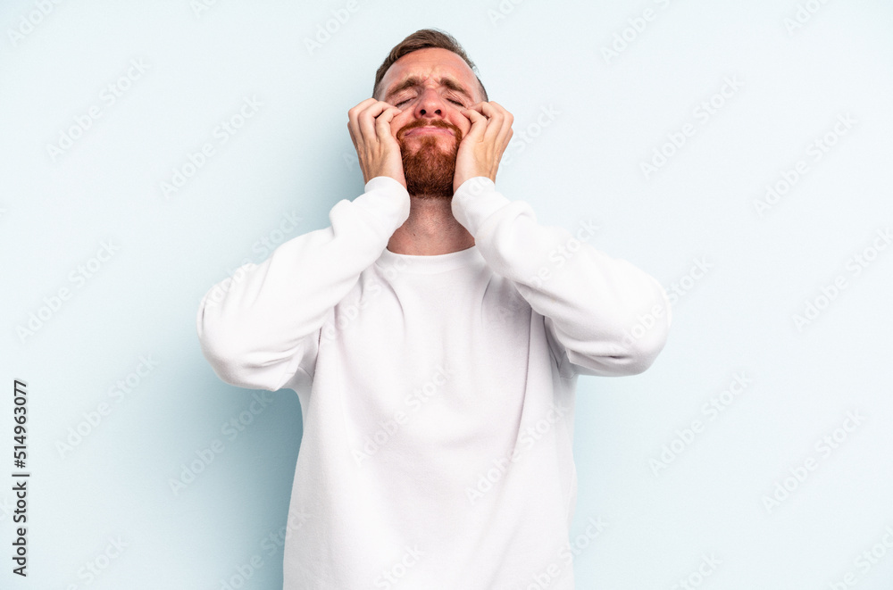 Young caucasian man isolated on blue background crying, unhappy with something, agony and confusion concept. Young caucasian man isolated on blue background crying, unhappy with something, agony and confusion concept.