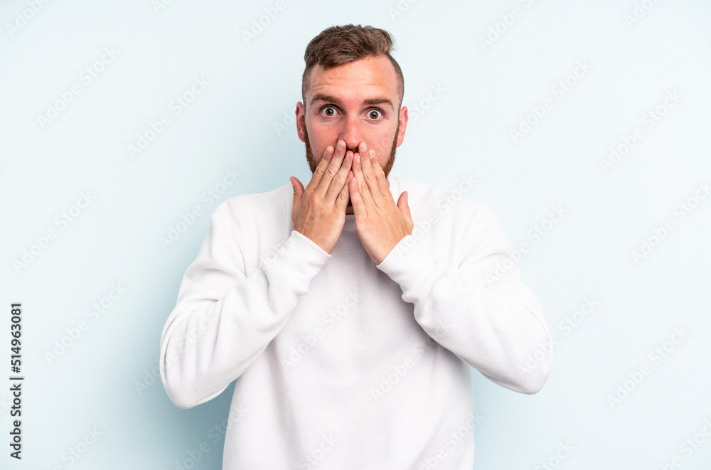 Young caucasian man isolated on blue background shocked, covering mouth with hands, anxious to discover something new. Young caucasian man isolated on blue background shocked, covering mouth with hands, anxious to discover something new.