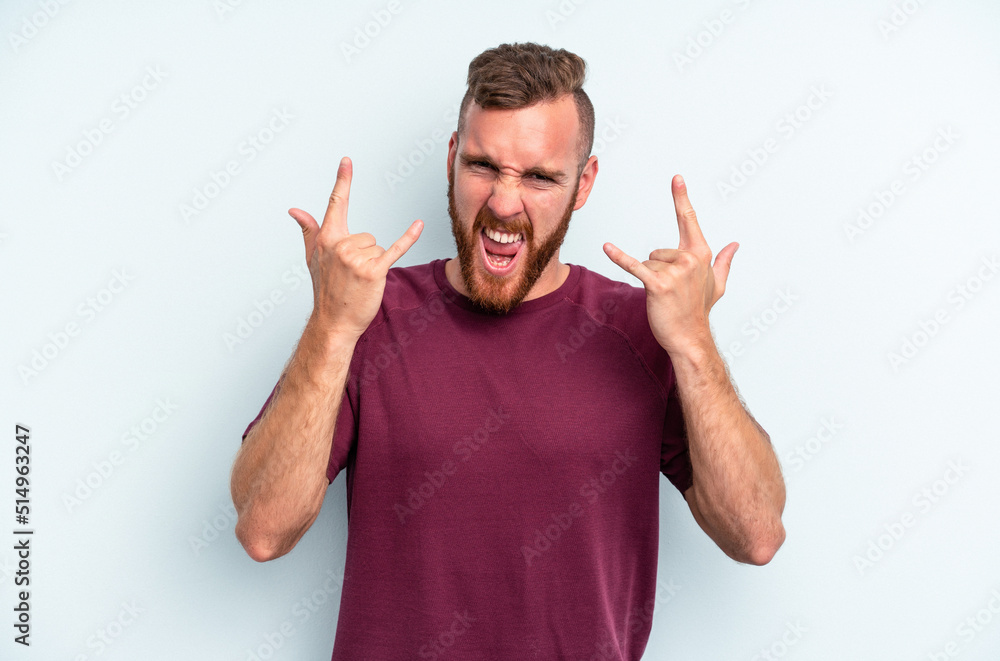 Young caucasian man isolated on blue background showing a horns gesture as a revolution concept. Young caucasian man isolated on blue background showing a horns gesture as a revolution concept.