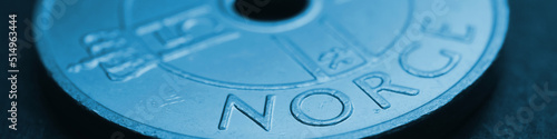 Translation: Norway. 1 Norwegian krone coin close up. National currency of Norway. Blue tinted money banner or header for news about economy or finance. Loan and credit. Tax and inflation. Macro photo