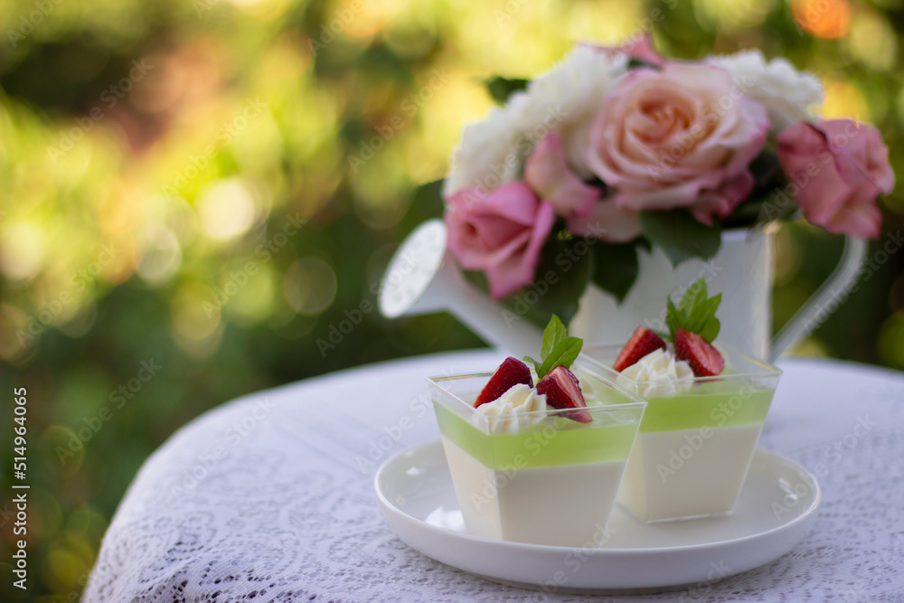 Panna cotta with lime  jelly and fresh strawberry. Dessert in a portion cups on a table in a coffee shop , rose flowers in a pot. Beautiful Desserts.