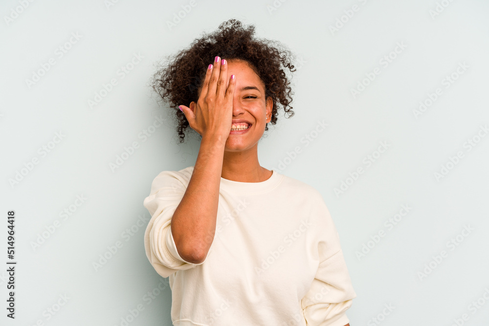 Young Brazilian woman isolated on blue background having fun covering half of face with palm. Young Brazilian woman isolated on blue background having fun covering half of face with palm.