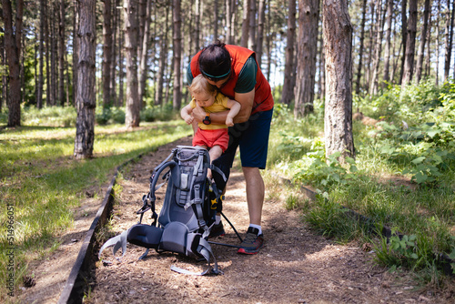 Young Caucasian father going on a hike with his baby daughter. He puts her in the baby carrier