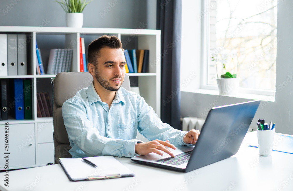 Young Man Works while Sitting in front of a Computer at Home. The Workplace of a Professional Worker, Freelancer or Student. Distance Work and Education Concept. Young Man Works while Sitting in front of a Computer at Home. The Workplace of a Professional Worker, Freelancer or Student. Distance Work and Education Concept.