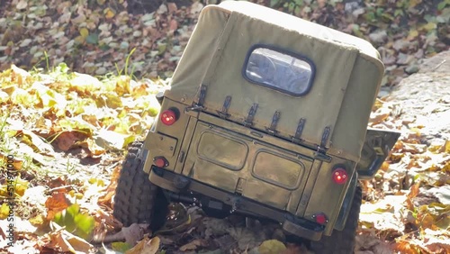 Radio control jeep in khaki colors drives on autumn leaves in a forest. Toy model of military vehicle outdoors.