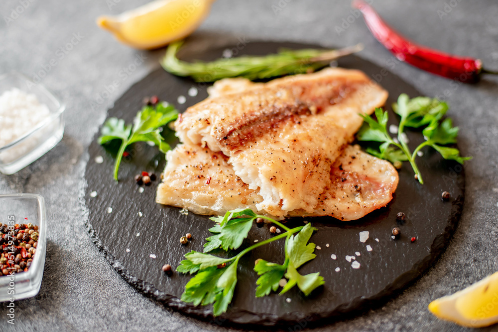 Baked white fish fillet Pangasius with spices and lemon on a stone background - obrazy, fototapety, plakaty 